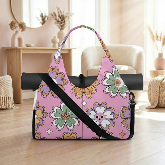A pink and green floral patterned tote bag with a black strap is placed on a wooden floor in a room with a mirror, vases, and a chair.
