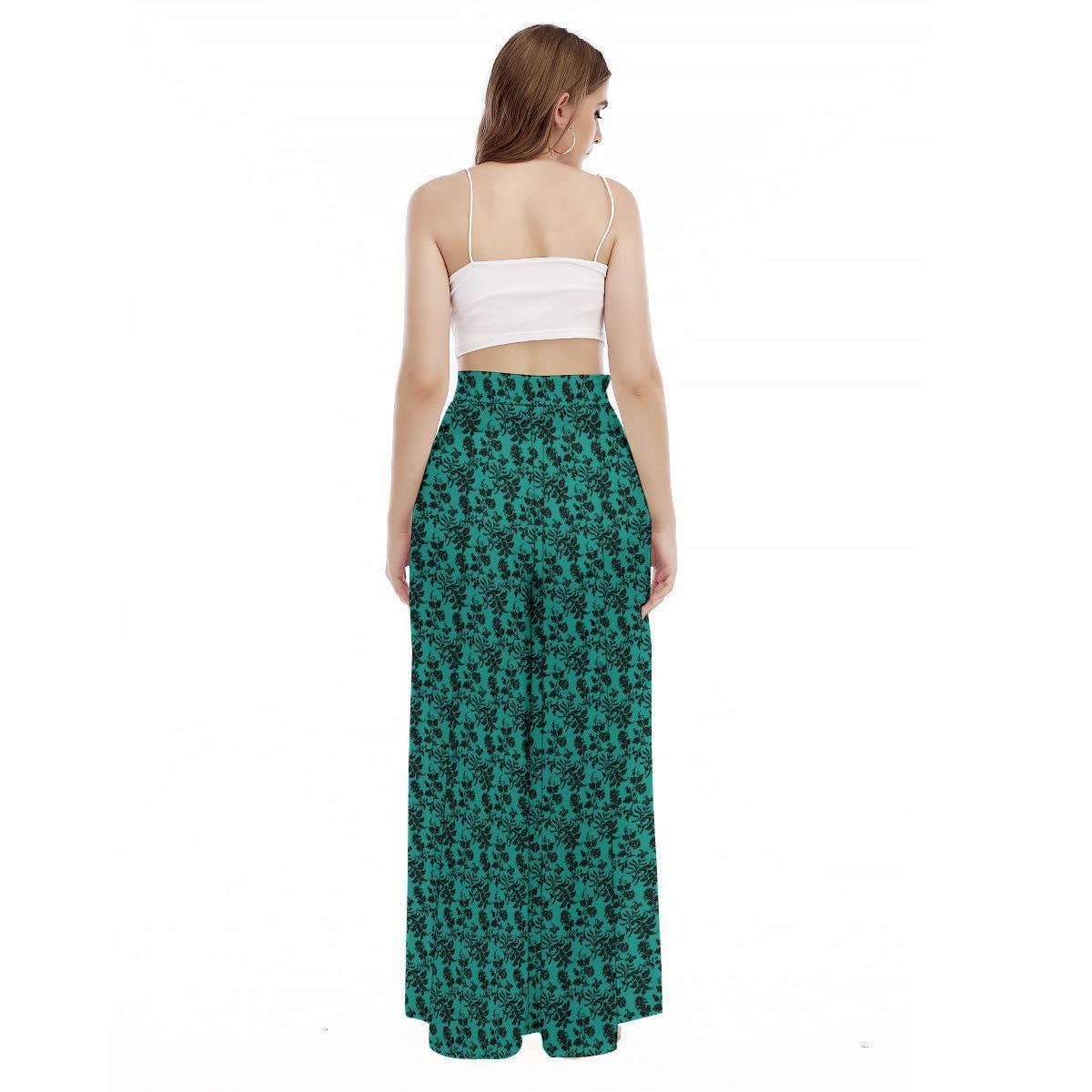 A rear view of a model wearing a white tank top and teal wide-leg pants covered in a black floral pattern.