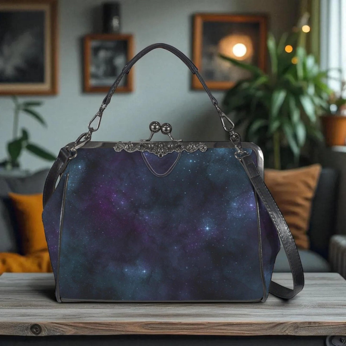 A handbag with a starry galaxy print design is displayed on a wooden surface, with a cozy indoor setting visible in the background.
