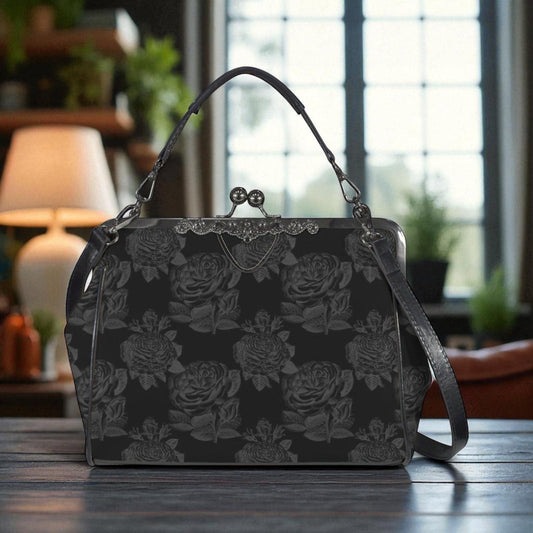 A black handbag with a floral pattern is displayed on a wooden surface, with a lamp and plants visible in the background.