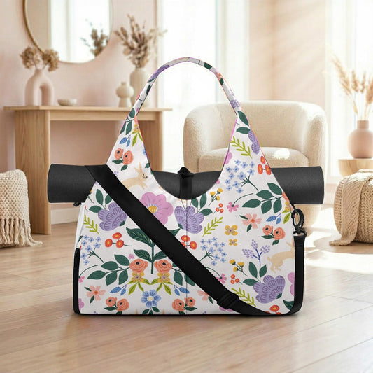 A colorful floral patterned tote bag with a black strap is displayed on a wooden floor in a room with a mirror, vases, and a chair.