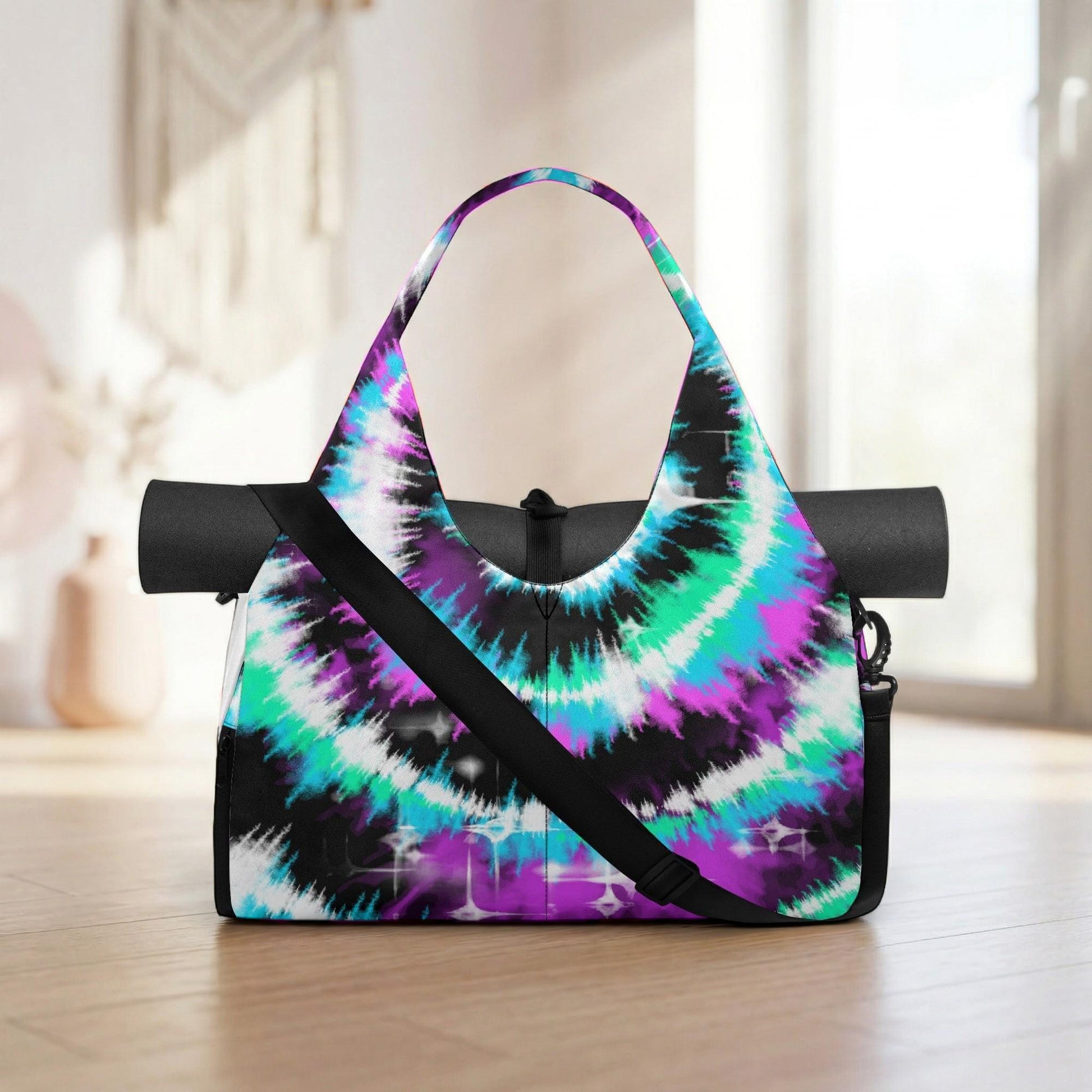 A colorful, tie-dye yoga bag with a black strap and handle is displayed on a wooden floor, with a window and a beige wall in the background.