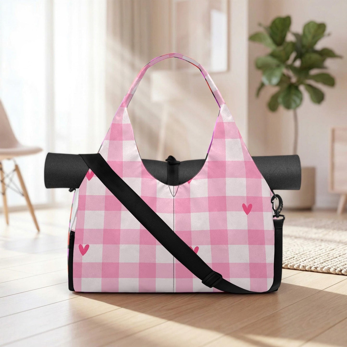 A pink and white checkered bag with a black strap and heart-shaped embellishments is placed on a wooden floor in a room with a potted plant in the background.