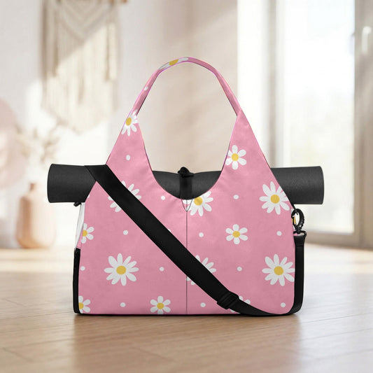 A pink tote bag with a floral pattern of white and yellow flowers, featuring a black strap and a black mat rolled up inside.