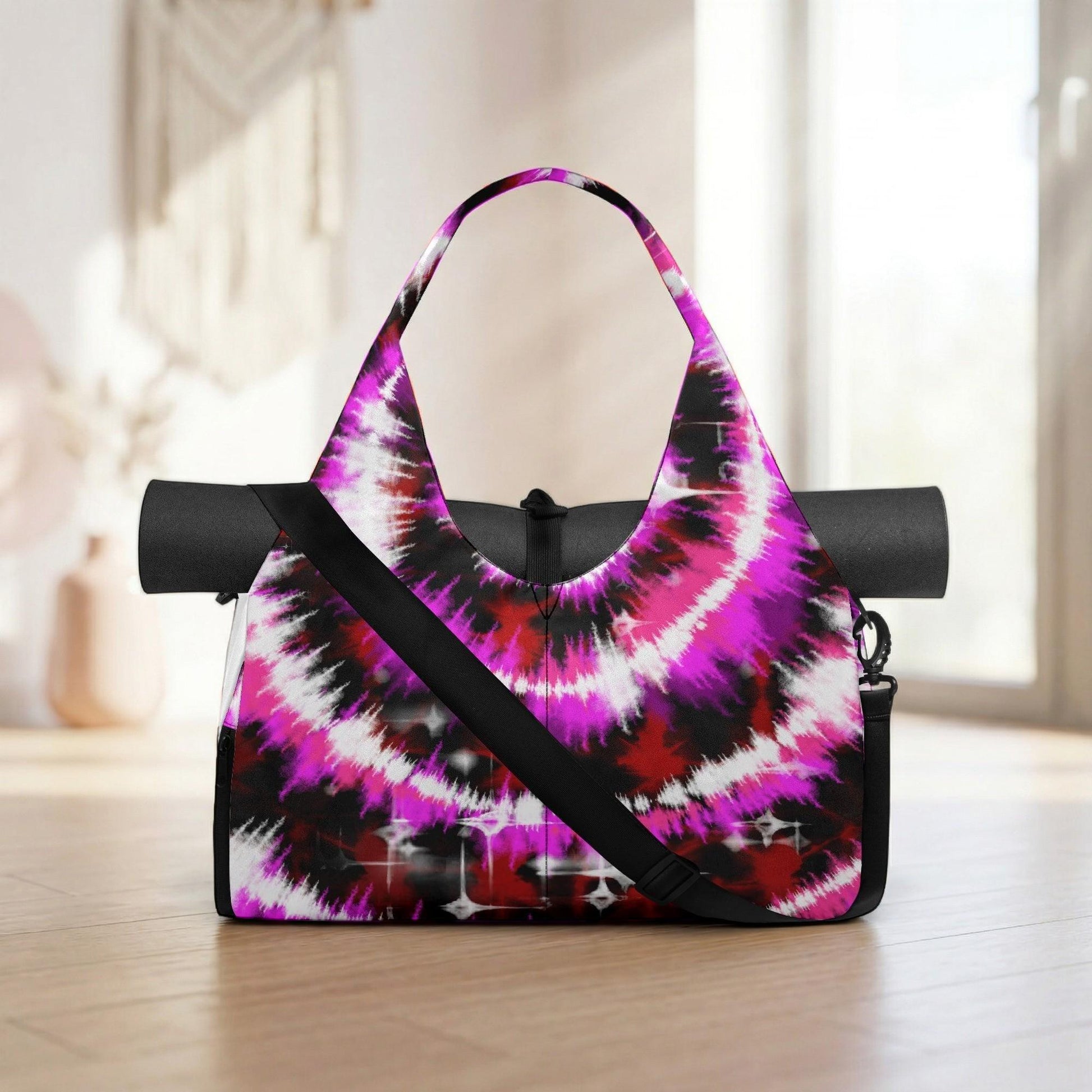 A colorful, tie-dye yoga bag with a black strap and a black mat rolled up inside, placed on a wooden floor.