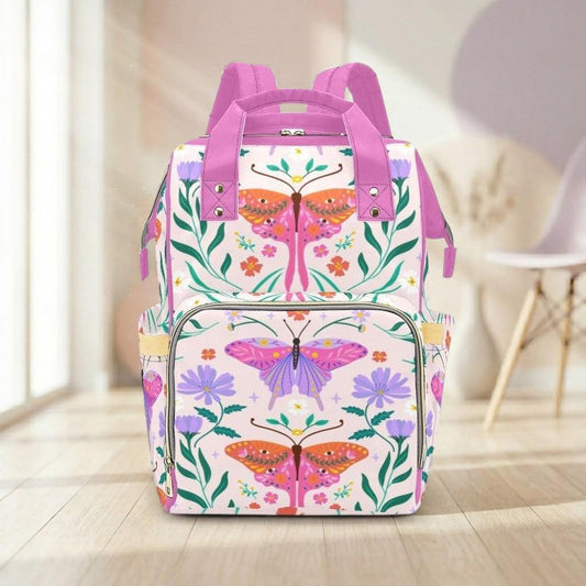 A colorful and vibrant backpack with a floral and butterfly design, featuring pink and purple colors, is displayed on a wooden floor against a white wall.