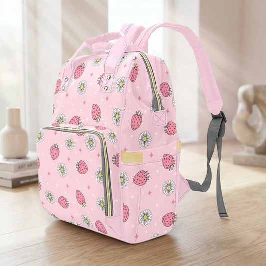 A pink backpack with a strawberry and daisy pattern is sitting on a wooden surface.