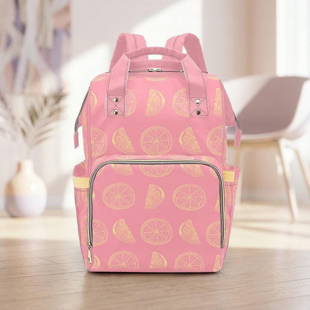 A pink backpack with a pattern of lemon slices on it, placed on a wooden floor in a room with a white chair and a vase in the background.