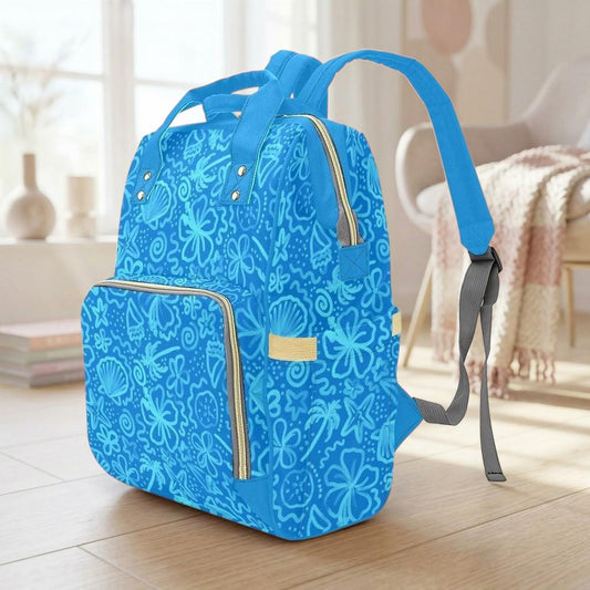 A blue backpack with a floral pattern is sitting on a wooden floor in a room with a window and a chair visible in the background.