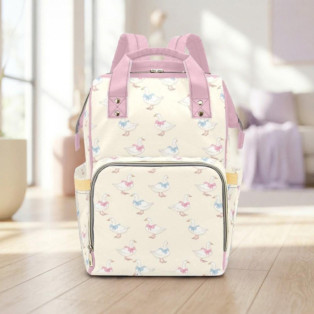 A pink and white patterned backpack with ducks printed on it, placed on a wooden floor against a white wall.