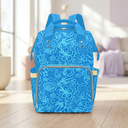 A blue backpack with a floral pattern is displayed on a wooden floor in a room with a window and a couch.