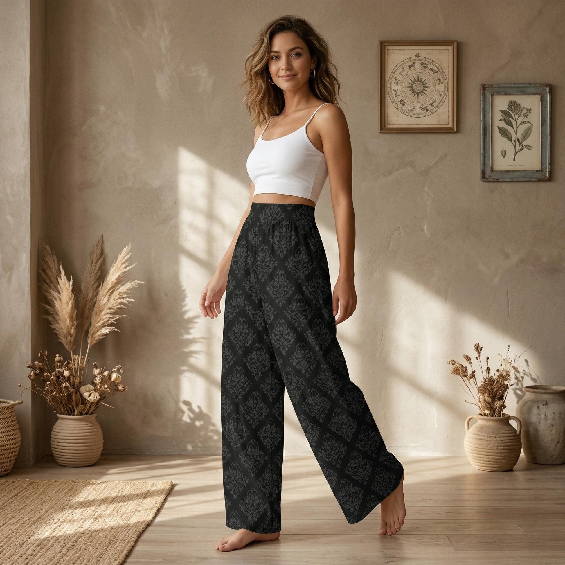 A woman wearing a white crop top and patterned wide-leg pants stands in a room with a neutral color palette, featuring potted plants and a framed artwork on the wall.