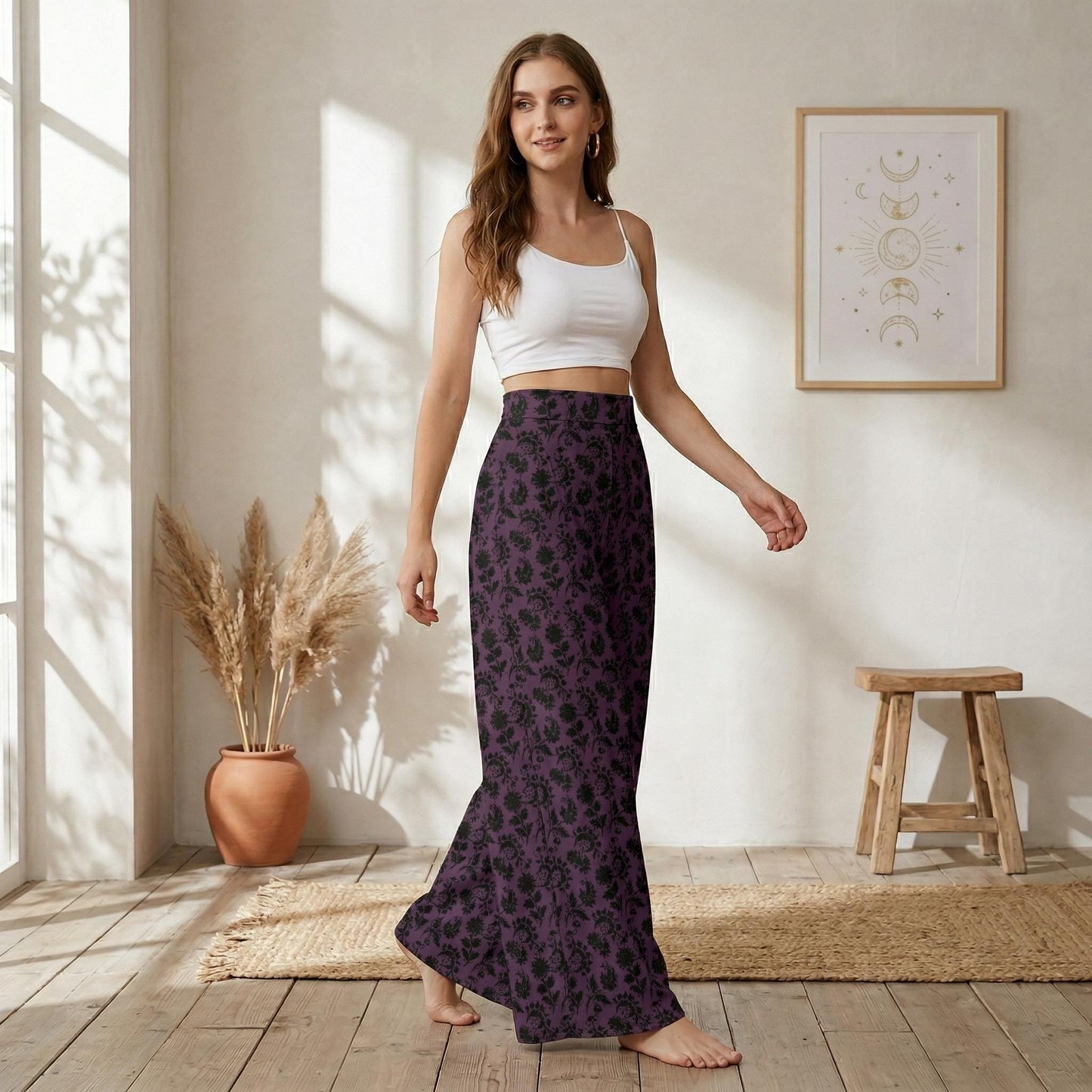 A woman wearing a white crop top and a long purple skirt with a floral pattern is standing in a room with a wooden stool and a potted plant.