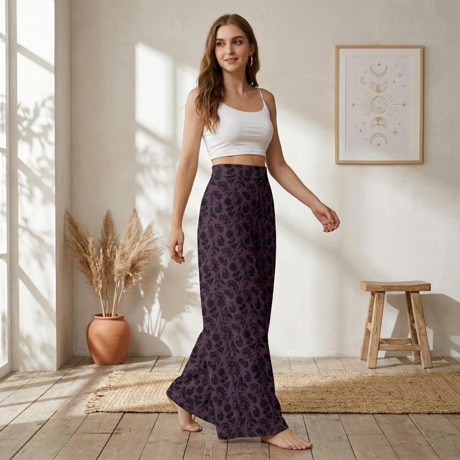 A woman wearing a white crop top and a long purple skirt with a floral pattern is standing in a room with a wooden stool and a potted plant.