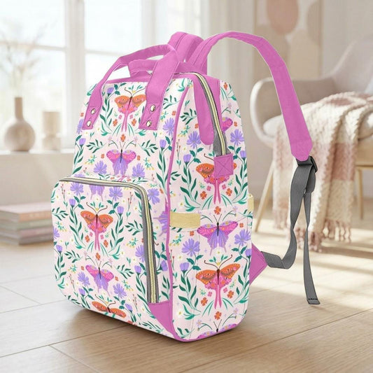 A colorful floral backpack with a pink strap is sitting on a wooden floor in a room with a window and a chair visible in the background.