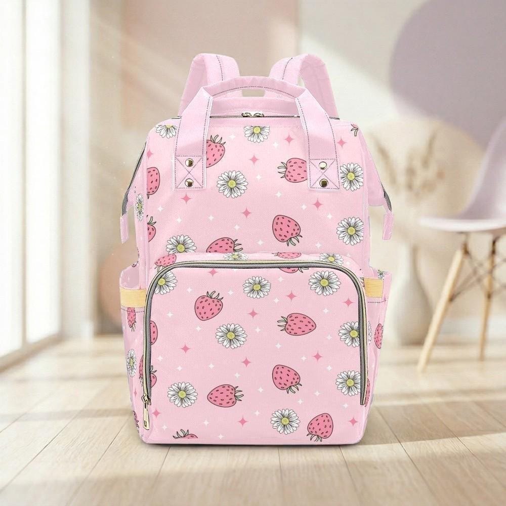 A pink backpack with a pattern of strawberries and daisies printed on it, placed on a wooden floor.
