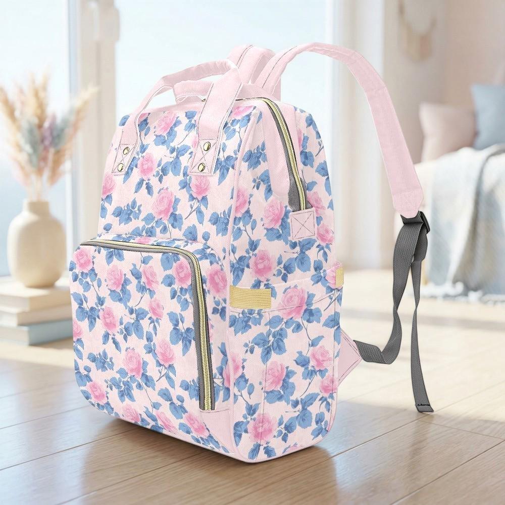 A pink floral backpack with a floral pattern sits on a wooden floor, with a vase of flowers in the background.