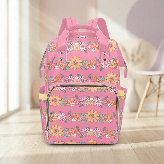 A pink backpack with a floral pattern is displayed on a wooden floor in a room with a chair visible in the background.
