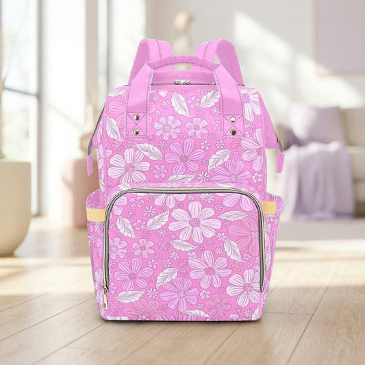 A pink floral backpack with a floral pattern is displayed on a wooden floor in a room with a window and a couch.