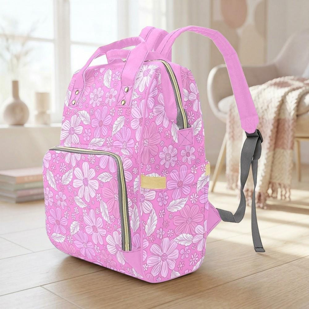 A pink floral backpack with a floral pattern is sitting on a wooden floor in a room with a window and a chair.