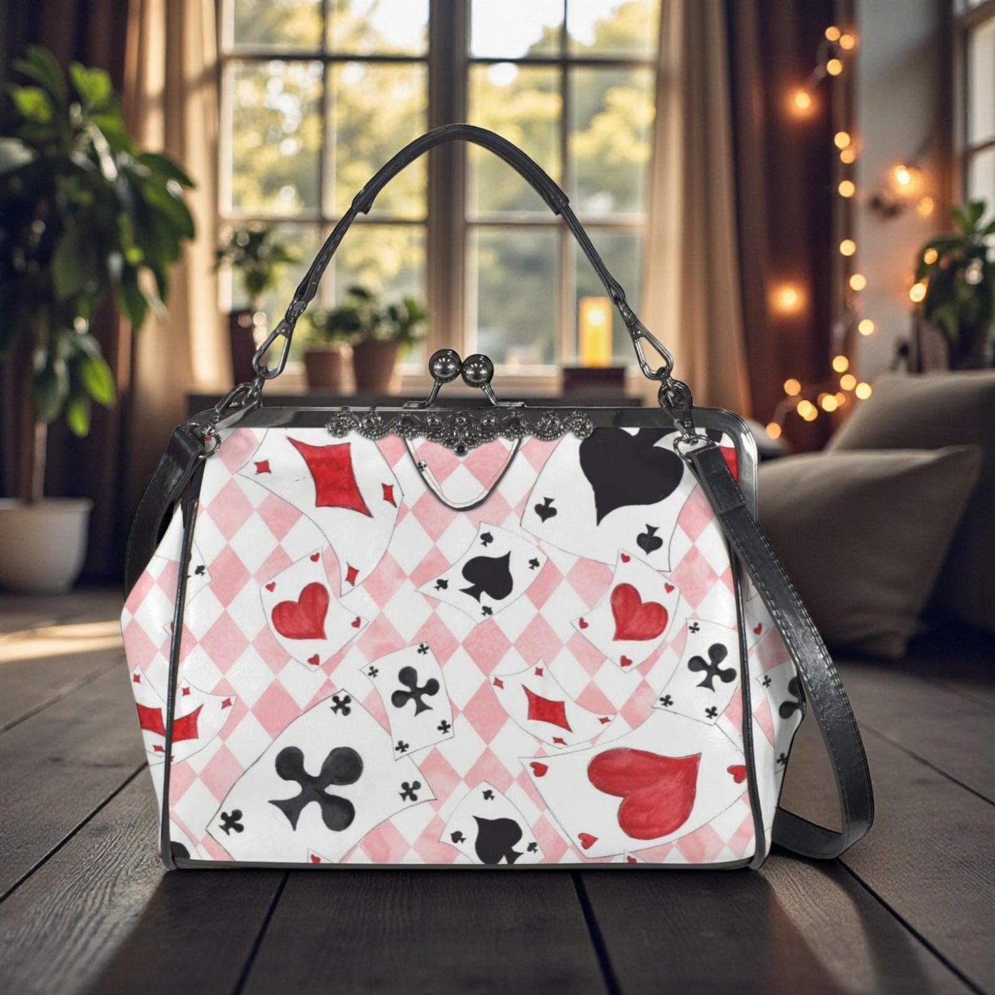 A handbag with a pattern of playing cards printed on it, sitting on a wooden surface in front of a window with string lights.