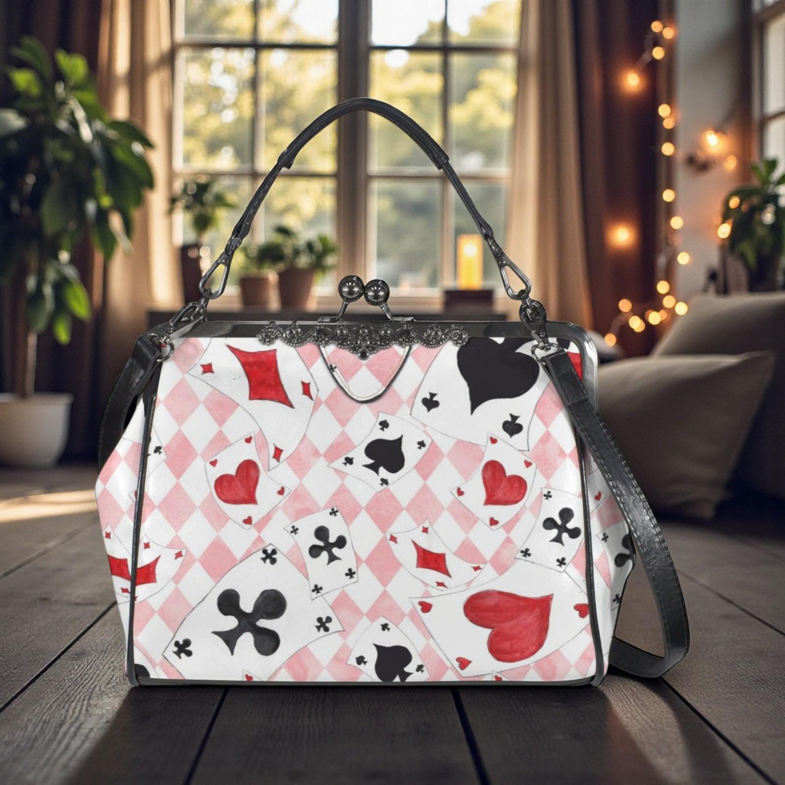 A handbag with a pattern of playing cards printed on it, sitting on a wooden surface in front of a window with string lights.