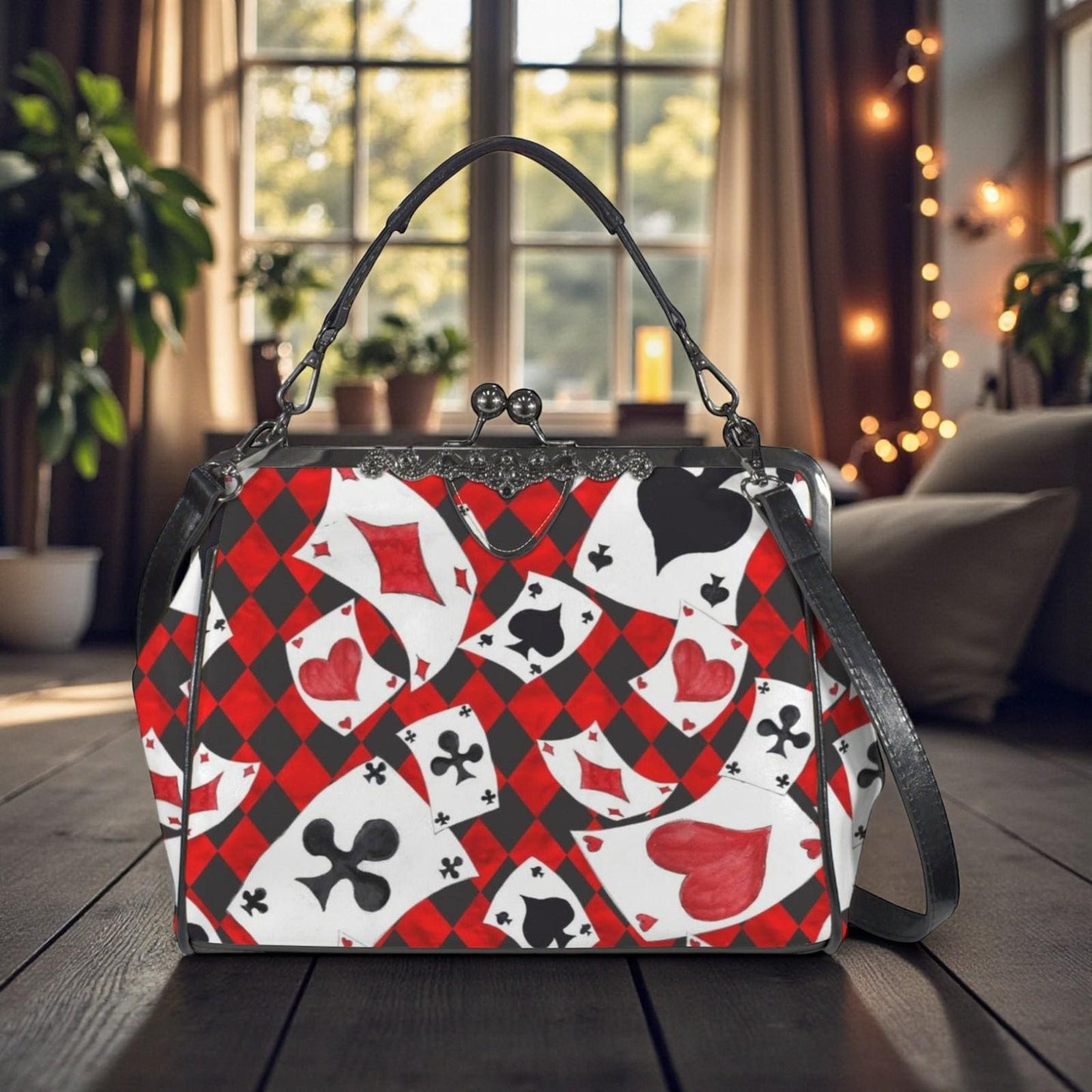 A handbag with a red and black pattern of playing cards is displayed on a wooden surface, with a window and plants visible in the background.