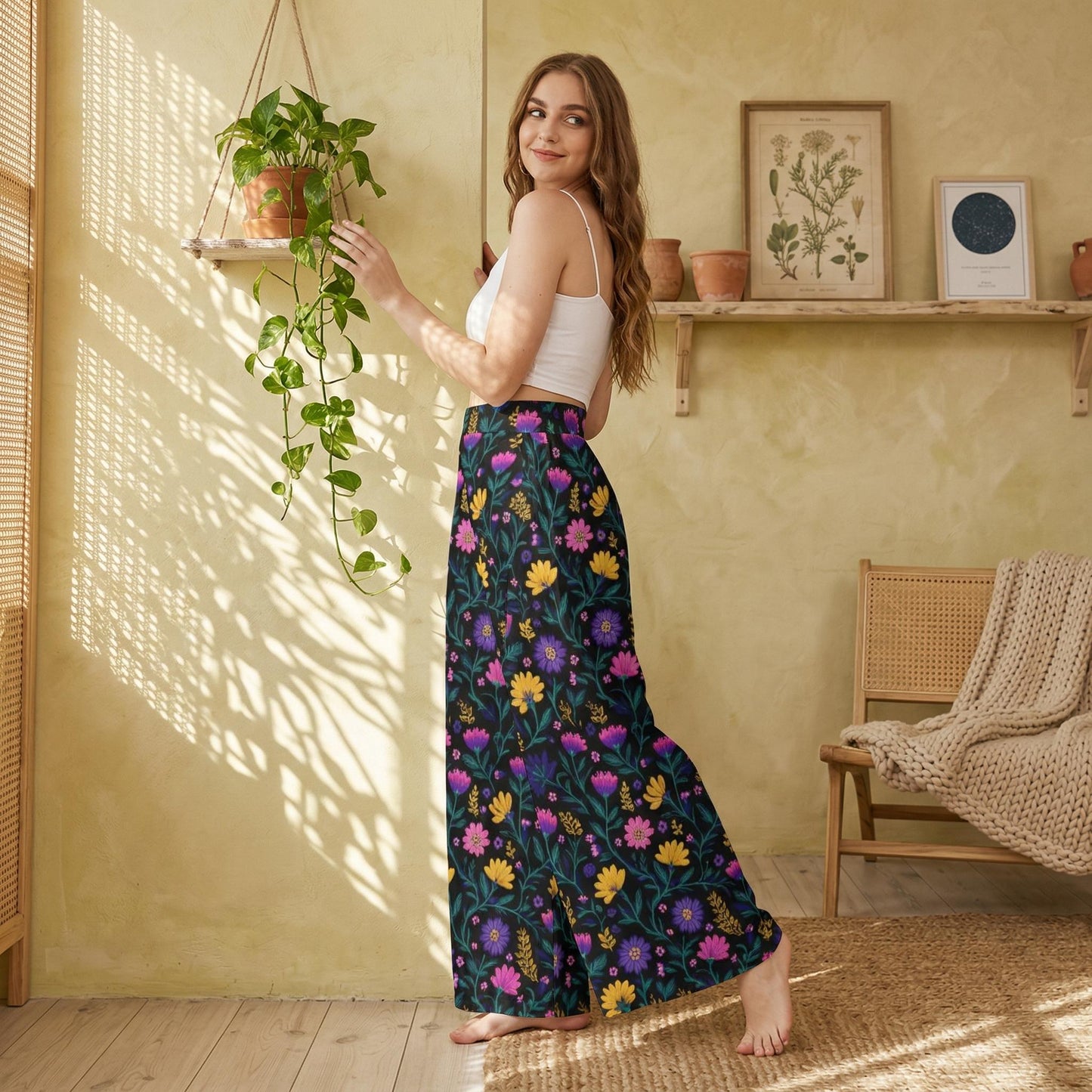A woman in a white crop top and a colorful floral skirt stands in a room with a potted plant, a shelf with framed pictures, and a woven chair.