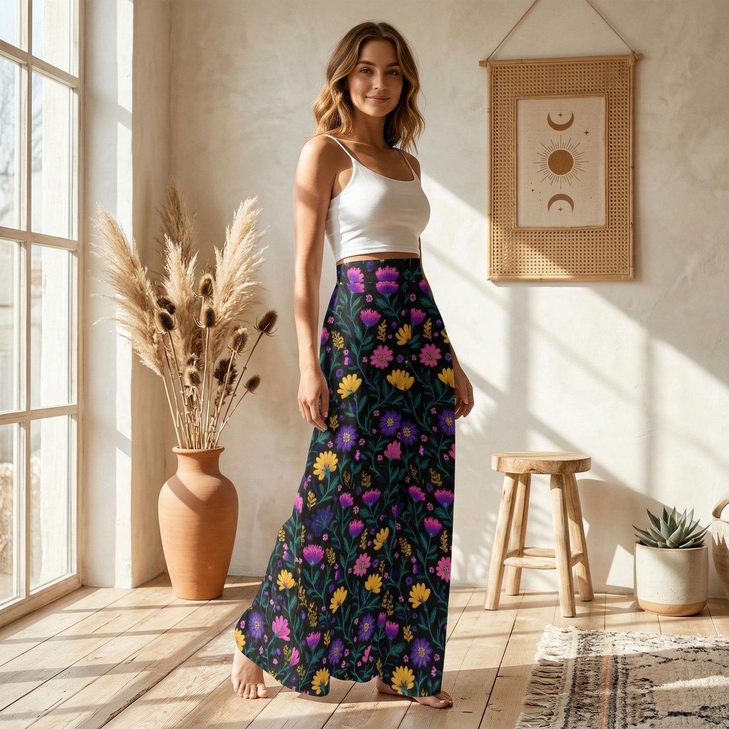 A woman wearing a white crop top and a long, colorful floral skirt stands in a room with a wooden stool, a potted plant, and a framed picture on the wall.