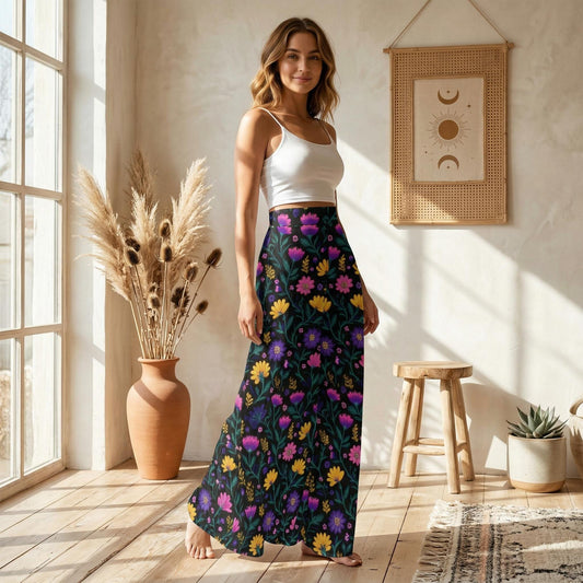 A woman wearing a white crop top and a long, colorful floral skirt stands in a room with a wooden stool, a potted plant, and a framed picture on the wall.