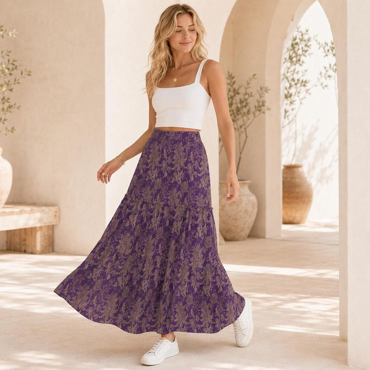 A woman wearing a white tank top and a purple damask maxi skirt, walking outdoors.