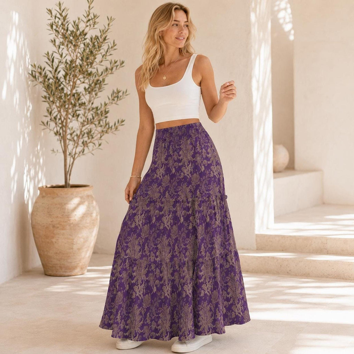 A woman standing outdoors in a white tank top and a purple floral tiered maxi skirt.
