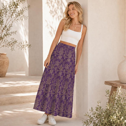 A woman leaning against a wall outdoors, wearing a white crop top and a purple patterned maxi skirt.