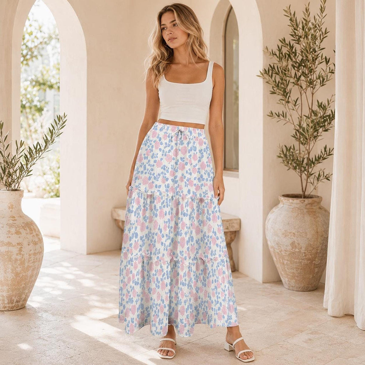 Full-length shot of the model wearing the white tank top and pink and blue patterned tiered maxi skirt in an arched hallway.