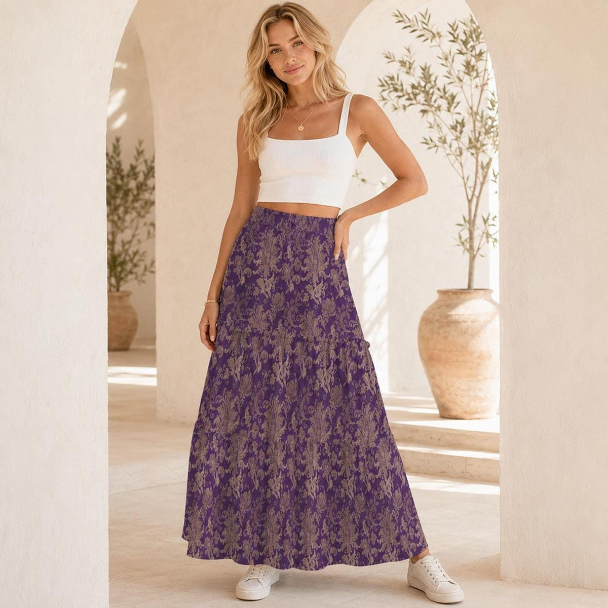 A woman posing with one hand on her hip, wearing a white crop top and purple patterned maxi skirt.