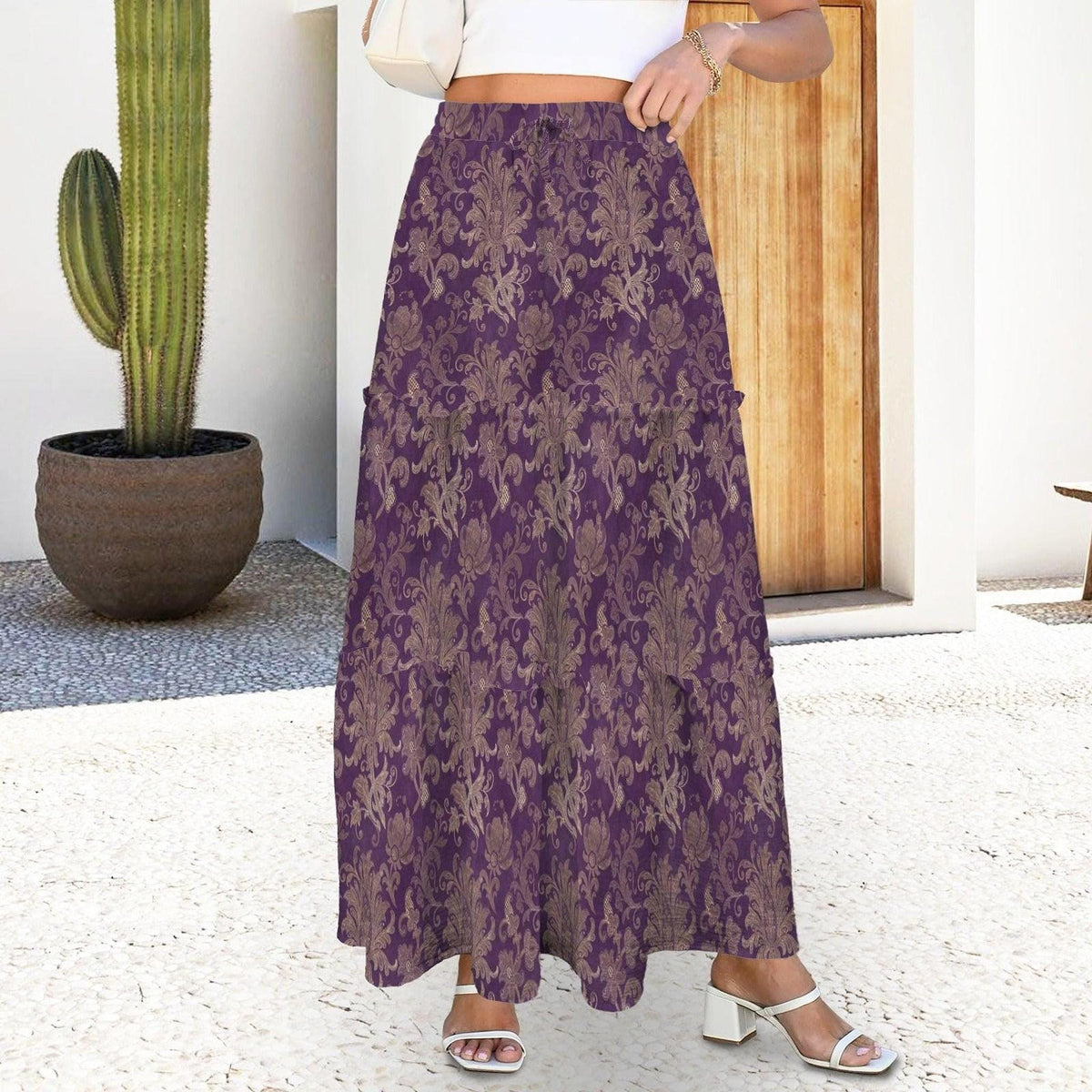 A cropped shot of a woman wearing a purple damask maxi skirt with white heeled sandals.