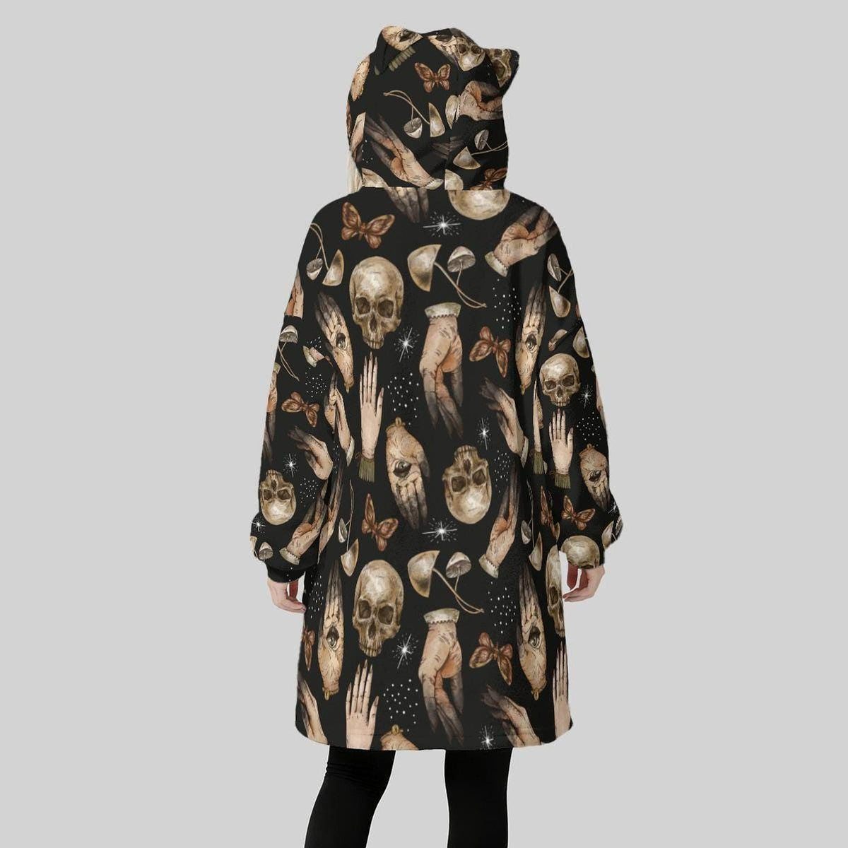 A person viewed from behind wears the black cat-ear hooded wearable blanket covered in a pattern of skulls, hands, and moths.