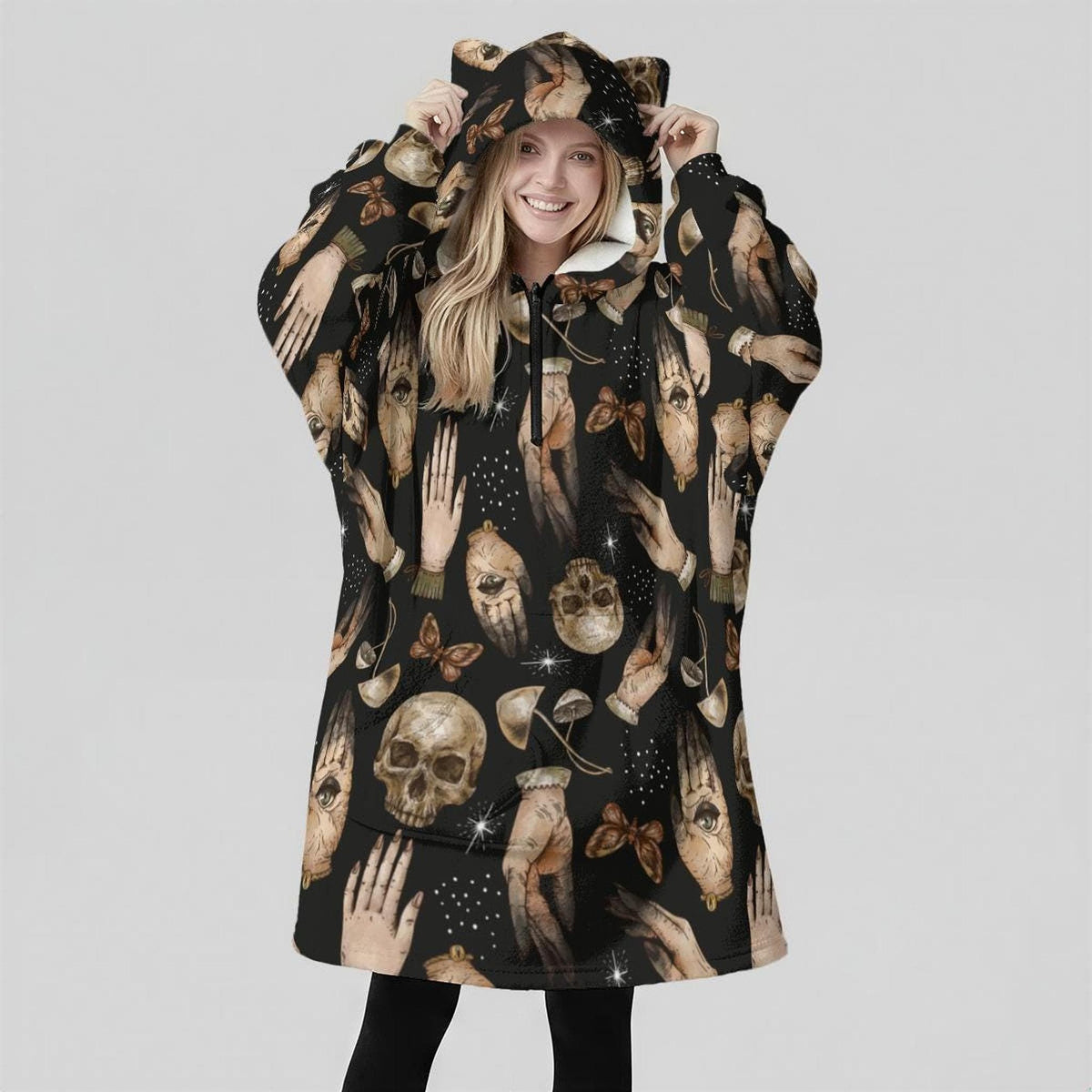 A woman facing forward wears an oversized black wearable blanket hoodie with cat ears on the hood and a skull pattern.