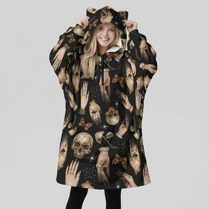 A woman facing forward wears an oversized black wearable blanket hoodie with cat ears on the hood and a skull pattern.