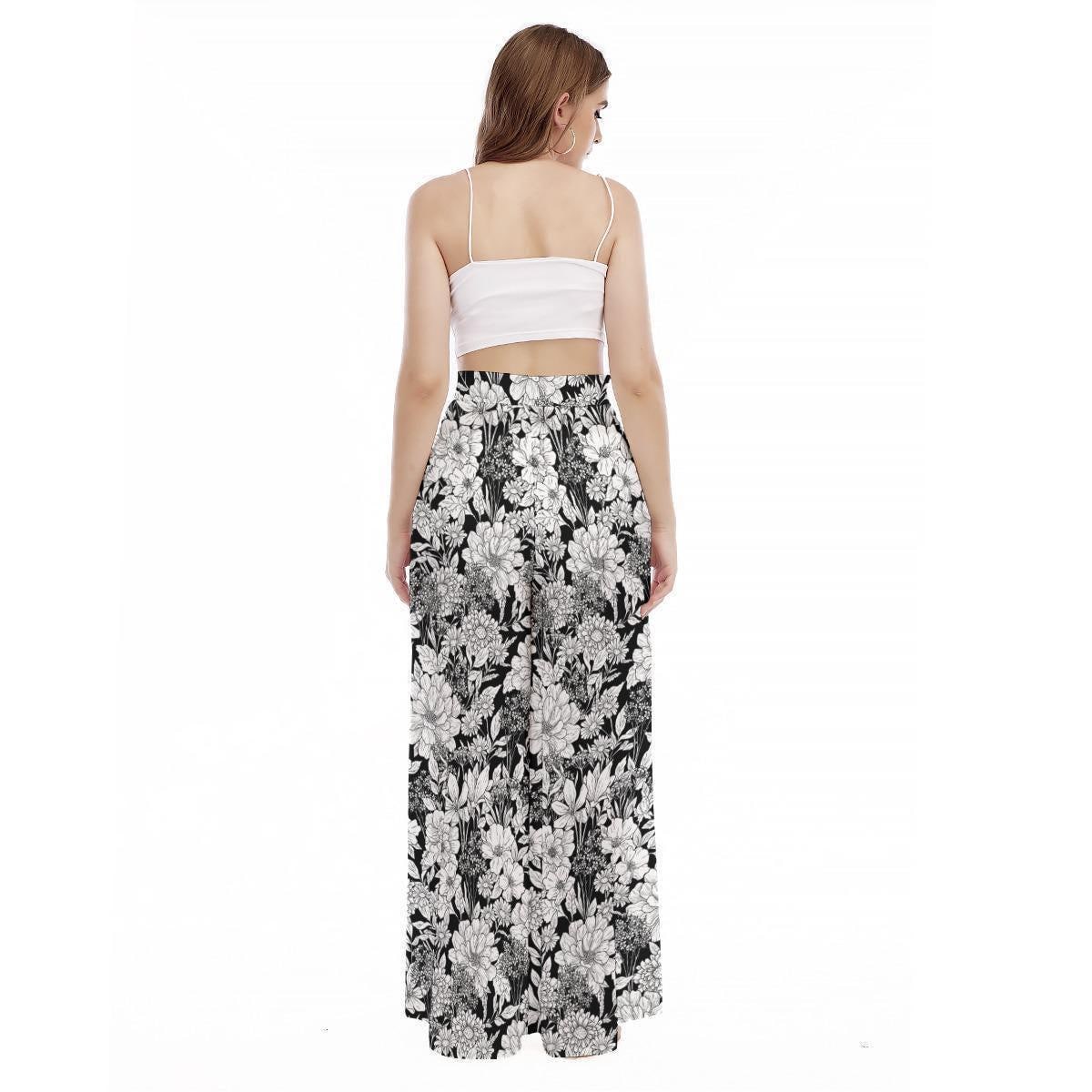 A woman seen from the back wears a white camisole and high-waisted black and white botanical print wide-leg trousers on a white background.